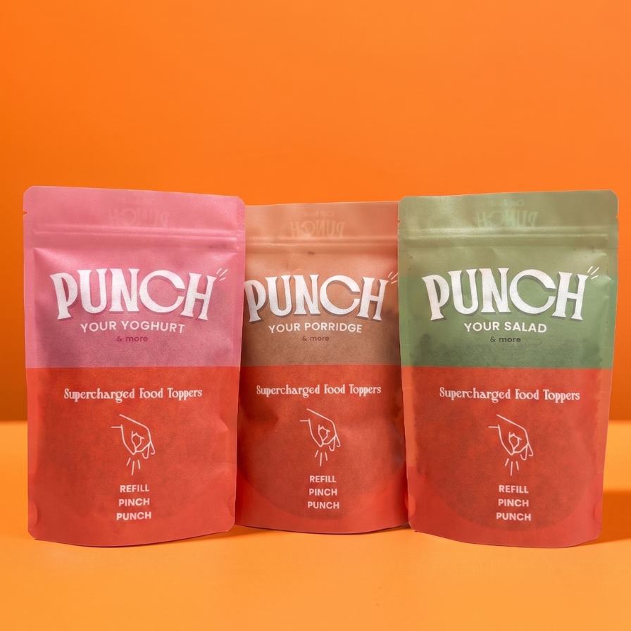 Three stand-up pouches of Punch brand food toppings arranged side by side against a solid orange background. The left pouch is pink, the middle is orange, and the right is green, each with the white 'PUNCH' logo and product text on the front.