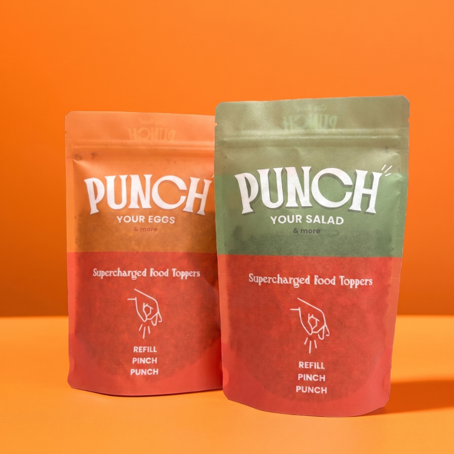 Two stand-up pouches of Punch brand food toppings on a solid orange background. The left pouch is peach and red with white text reading 'PUNCH YOUR EGGS' and 'Supercharged Food Toppers'.