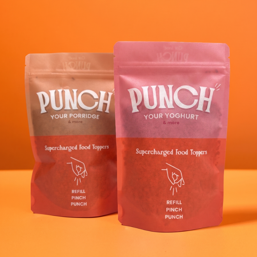 Two stand-up pouches of Punch Your Porridge & Yoghurt Supercharged Food Toppers on an orange background. The pouch on the left is a light brownish-pink, and the pouch on the right is a dusty rose pink, both with white branding and text.