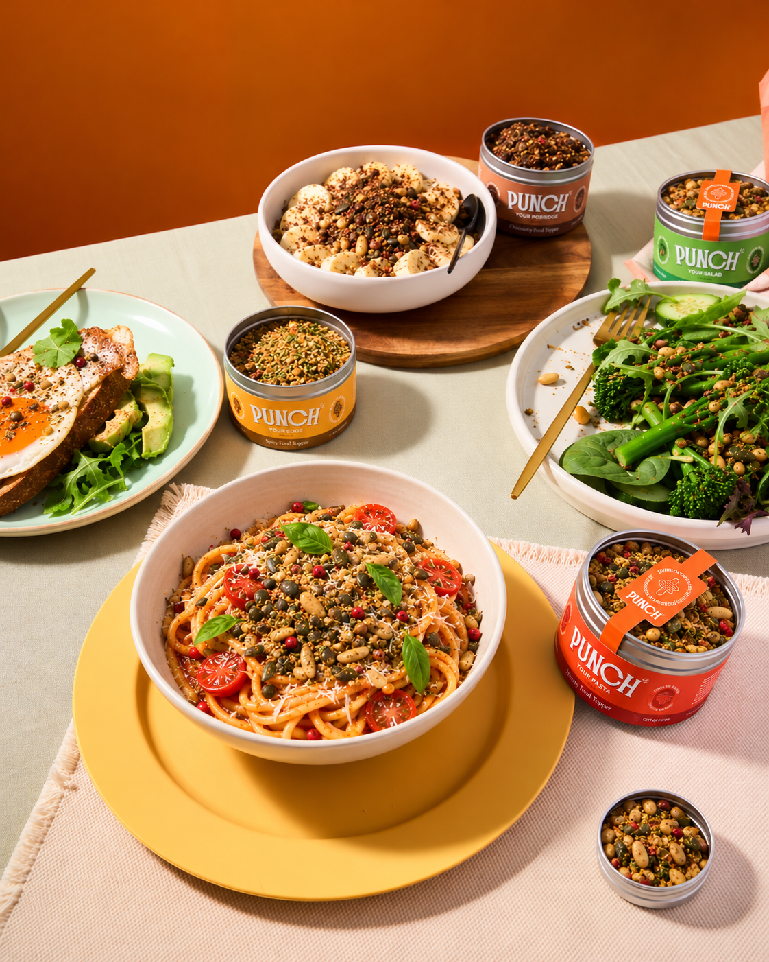 A styled tabletop food scene showing bowls and cans of PUNCH protein powder mixed into pasta, salad, and a breakfast toast. The PUNCH branding is clearly visible on the cans, set against a warm orange wall and beige table setting.