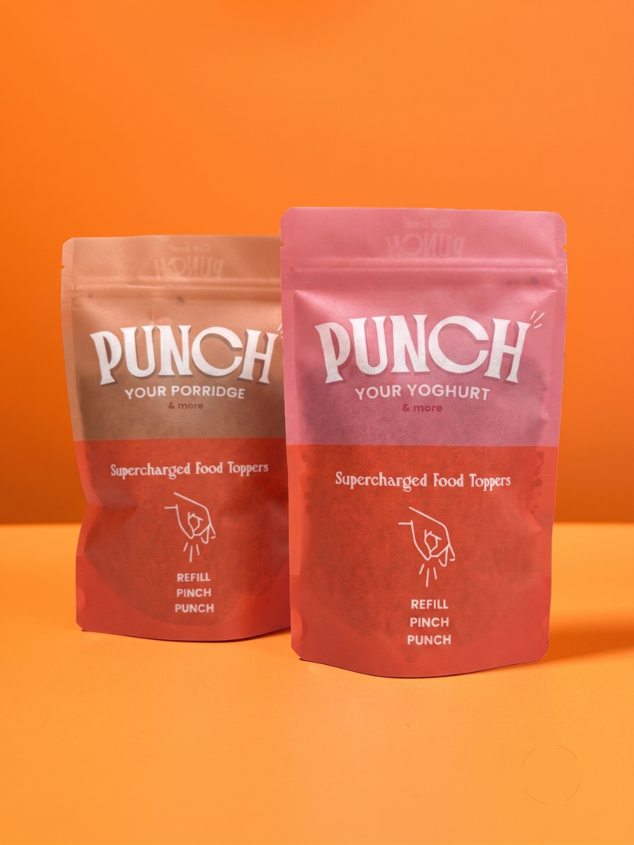 Two stand-up pouches of Punch Your Porridge & Yoghurt Supercharged Food Toppers on an orange background. The pouch on the left is a light brownish-pink, and the pouch on the right is a dusty rose pink, both with white branding and text.