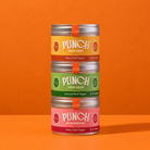Three stacked metal tins of PUNCH food toppings on a solid orange background. The tins are labeled Spicy Food Topper, Savoury Food Topper, and Fruity Food Tipper, with yellow, green, and pink labels respectively.
