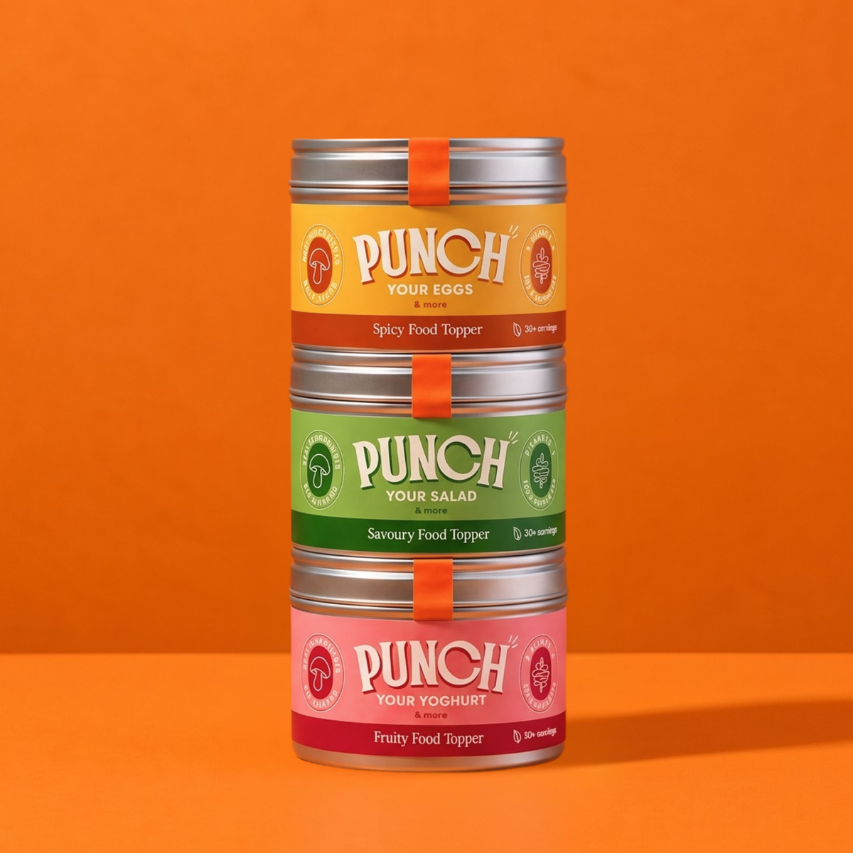 Three stacked metal tins of PUNCH food toppings on a solid orange background. The tins are labeled Spicy Food Topper, Savoury Food Topper, and Fruity Food Tipper, with yellow, green, and pink labels respectively.
