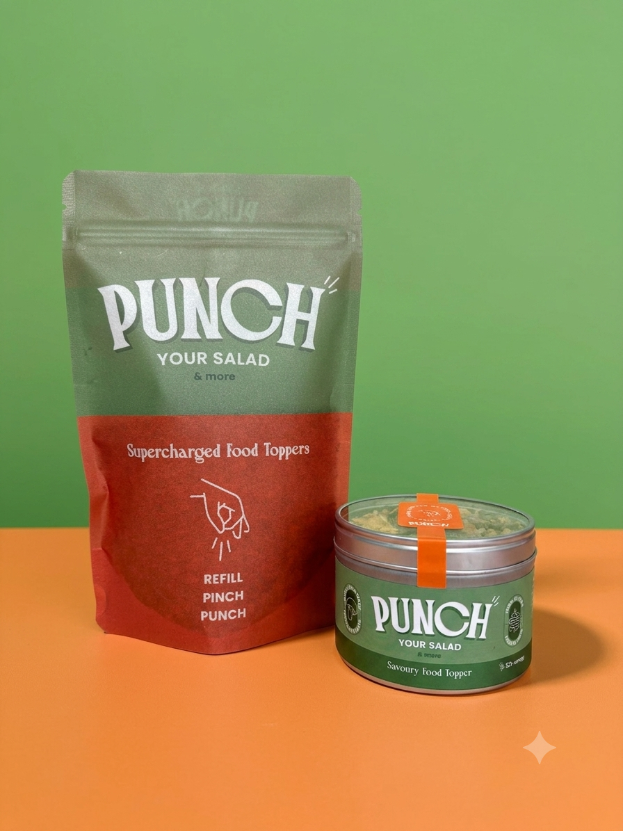 A pouch and a small round tin of PUNCH Your Salad supercharged food toppers on a two-tone green and orange background. The pouch is olive green and red, and the tin is green with a small orange seal.